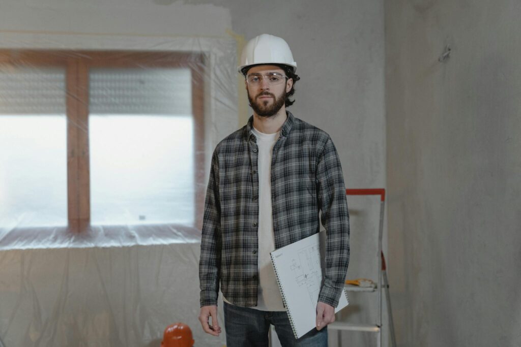 Adult male construction worker holding blueprints in an indoor renovation site.