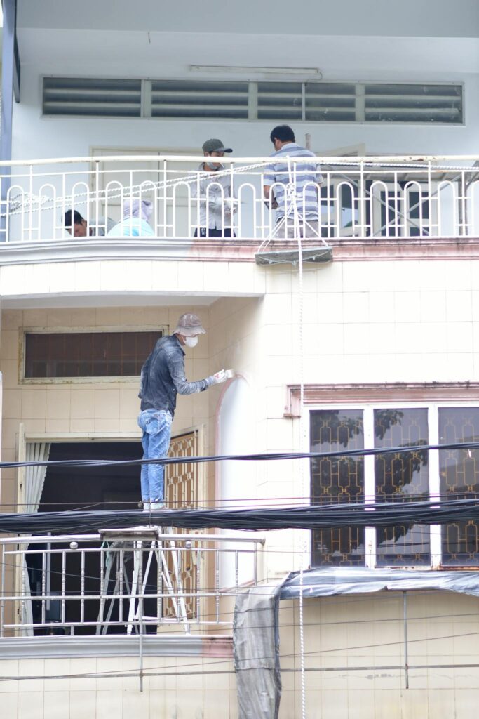 Construction workers painting and renovating a building facade, captured outdoors during daytime.